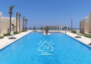 a swimming pool in a resort with palm trees and the ocean at Taj Home ,cozy mangroovy 2BR apartment..pool&Beach access in Hurghada