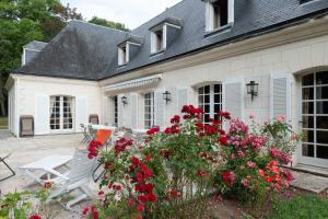 uma casa branca com flores vermelhas no quintal em Spacious house in a wooded park enclosed by walls and its swimming pool em Saint-Cyr-sur-Loire