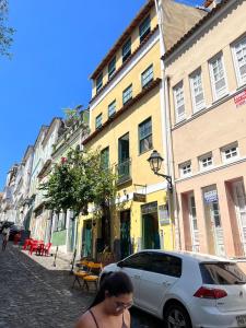 a woman walking down a street next to a white car at Tamboleiro's Hotel Residence in Salvador