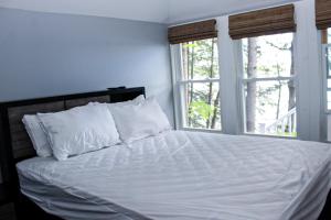 a bedroom with a white bed with two windows at Lake Winnisquam Getaway in Sanbornton