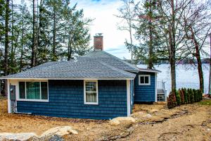 a small blue house in front of the water at Lake Winnisquam Getaway in Sanbornton