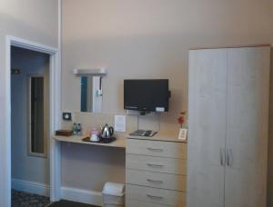 a bedroom with a desk with a television and a cabinet at Melbourne Guest House in Rhyl