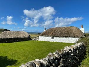 dos edificios con techo de paja en un campo con una pared de piedra en Beaton's Croft House - Uig Skye, en Portree