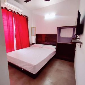 a bedroom with a bed with red curtains and a tv at Sea Nest in Alibaug