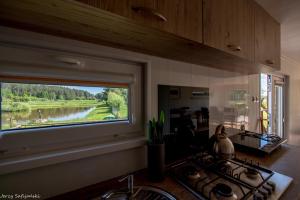 a kitchen with a window with a view of a river at Wilimy, Domek Przy Stawie in Biskupiec