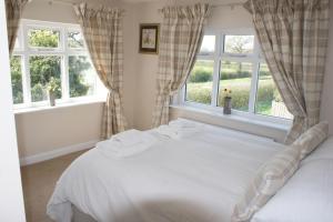 a bedroom with a white bed with two windows at Spacious 4 bed family cottage in parkland setting in York