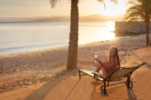 una mujer sentada en una silla en la playa en Mövenpick Resort & Residences Aqaba, en Áqaba