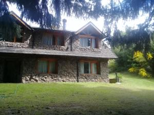 a stone house with a grass yard in front of it at LA Nevadita, Chalet cabin located near the center- It includes suite room with double bed and another 2 bedrooms with two singles beds- Living room fireplace, Hot water, WI-FI in Villa La Angostura