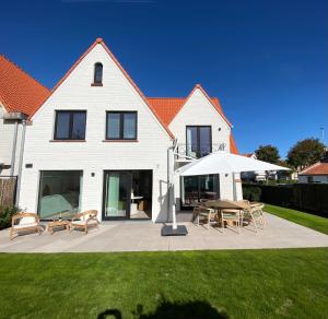 a white house with a table and chairs and an umbrella at House Santa Maria - North Sea Stays in De Haan