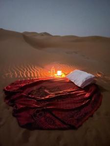 ein Bett mitten in der Wüste mit einer Kerze in der Unterkunft Erg Chegaga Camp & Activites in M’hamid El Ghizlane