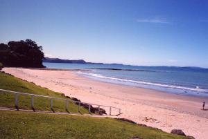 a sandy beach with a metal railing next to the ocean at Red Beach Garden Cottage in Red Beach