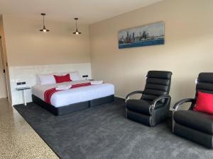 a bedroom with a bed and two chairs at Matakana Motel in Matakana
