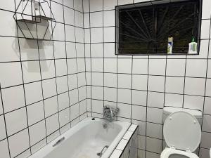 Maponya Guest House في Pimville: حمام من البلاط الأبيض مع حوض استحمام ومرحاض