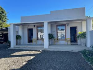 a white building with yellow chairs in front of it at Back Home Bed and Breakfast in Graaff-Reinet