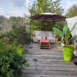 une terrasse en bois avec un parasol, un canapé et des chaises dans l'établissement TENTE SAFARI LODGE DANS FORET LUXURIANTE, à Vielle-Tursan