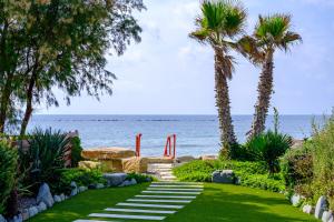 a garden with palm trees and a pathway next to the ocean at The MedView Garden House in Pervolia