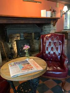 a table with a newspaper and a chair with a fireplace at John Barleycorn in Duxford