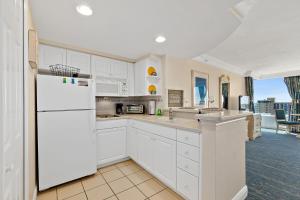 a kitchen with white cabinets and a white refrigerator at Sunshine Beach Condo with Balcony Pool Hot Tub in Daytona Beach