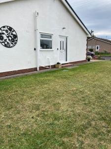 a white house with a window and a grass yard at 17 Cheerful 2 bed bungalow, hot tub/gym/pool table in Prestatyn