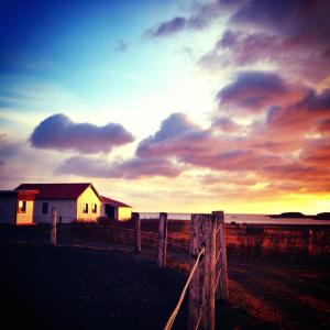 a house on the beach with a fence and the sunset at Dynjandi Guesthouse in Höfn