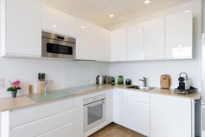 a white kitchen with white cabinets and stainless steel appliances at Les Oules Vertes YourHostHelper classé 3 étoiles in Théoule-sur-Mer