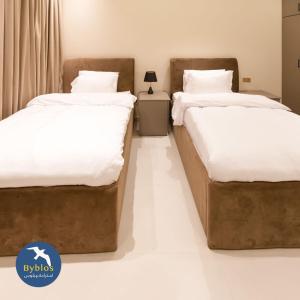 two beds in a room with white sheets at Byblos Villa Resort in Al Ḩadd