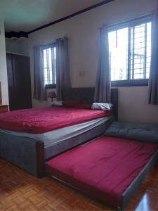 two beds in a bedroom with red sheets and windows at Balili Property at Metro Manila Hills Subd Rodriguez Rizal in Manila