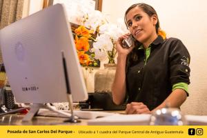 a woman talking on a cell phone in front of a computer at Posada de San Carlos del Parque in Antigua Guatemala