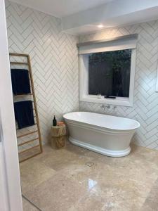 uma casa de banho branca com uma banheira e uma janela em Sunnyside Luxurious 4BR Art Villa, Fireplace, Village 2mins em Wentworth Falls