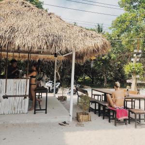 un grupo de personas sentadas en bancos bajo un paraguas de paja en Tropical Hostel en Ko Phayam