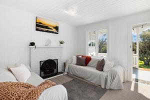 a white living room with a fireplace and a couch at Karitane Cottage - Karitane Holiday Home in Karitane