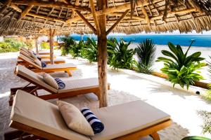 a beach with chairs and a straw umbrella and the ocean at Alladin Boutique Beach Hotel and SPA Zanzibar in Matemwe