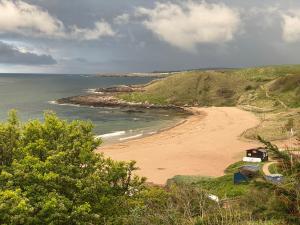 a beach with a house on a hill next to the ocean at 1 The Bay - Stunning contemporary flat on the Scottish coast in Coldingham
