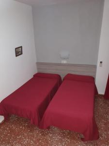 two beds in a room with red sheets at Pensión los Ángeles in La Puebla de Cazalla