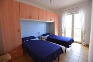 two beds in a bedroom with blue sheets and a window at Lina apartments in Ginosa Marina