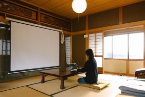 una mujer sentada en el suelo frente a una mesa con un portátil en Lacomaゲストハウス, en Esumi