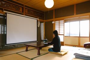 a woman sitting on the floor in front of a table with a laptop at Lacomaゲストハウス in Esumi