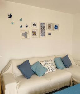 a white couch with blue pillows and pictures on the wall at Casa da Boa Gente in Cabanas de Tavira