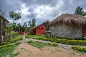 a building with a straw roof and a building with a pathway at Deshadan Eco Valley Resort - An Eco friendly Mud House in Kanthalloor