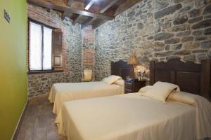 a bedroom with two beds and a stone wall at Apartamentos El Aramo Asturias in Pola de Lena
