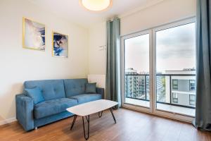 a living room with a blue couch and a large window at Wola Lush Apartment in Warsaw