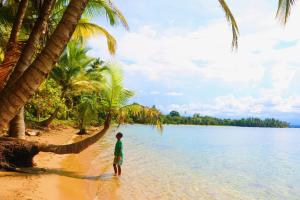 a boy standing on a beach with palm trees at Castillo Inspiracion Hostel in Bocas del Toro