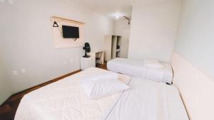 two beds in a white room with a tv at Nacional Hotel Coral in Lages