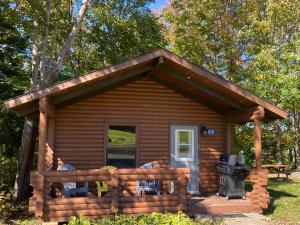 a log cabin with a porch and a grill at Adventures East Cottages and Campground in Baddeck Inlet