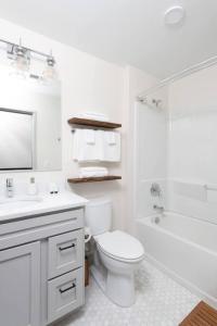 a white bathroom with a toilet and a tub and a sink at Brewery District 2-Story 2BR Apt Near Fiserv with Rooftop, Gym, and Parking in Milwaukee +19 photos
