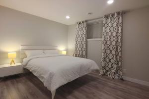 a white bedroom with a bed and a window at Beautiful 2 bedroom + office basement suite in Calgary