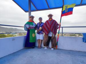 tres personas de pie en un balcón sosteniendo una bandera en Hostal Alcazaba, en Puerto López