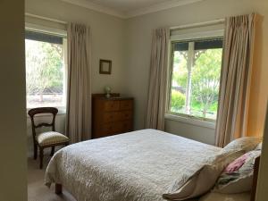 a bedroom with a bed and a chair and two windows at Belle B&B Country Retreat in Penwortham
