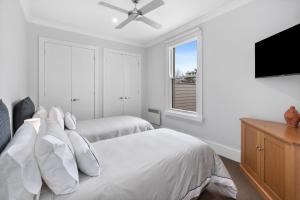a white bedroom with two beds and a flat screen tv at The SCOOP in Queenscliff