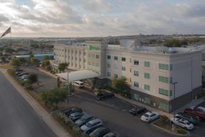 un grande edificio bianco con auto parcheggiate in un parcheggio di Holiday Inn Hotel & Suites Northwest San Antonio, an IHG Hotel a San Antonio